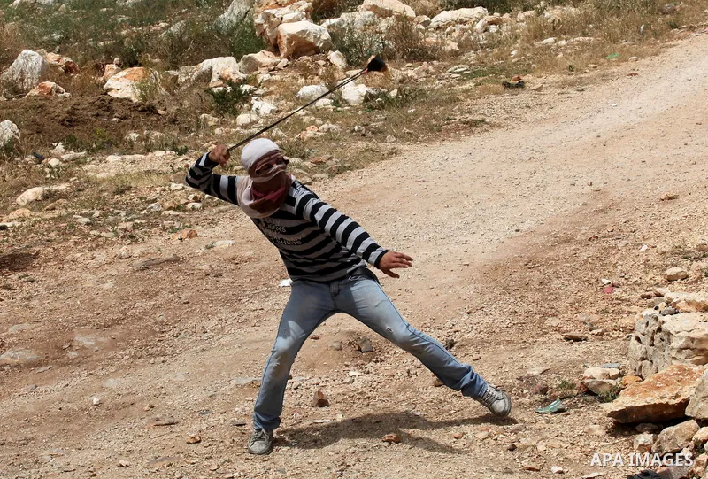 A Palestinian protester uses a slingshot to hurl stones towards Israeli security forces during clashes following a demonstration against the expropriation of Palestinian land by Israel, on May 13, 2016 in the village of...