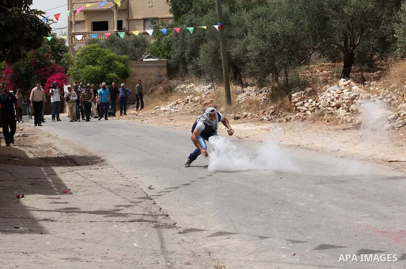 A Palestinian protester hurls a tear gas canister back towards Israeli security forces during clashes following a demonstration against the expropriation of Palestinian land by Israel, on May 13, 2016 in the village of K...