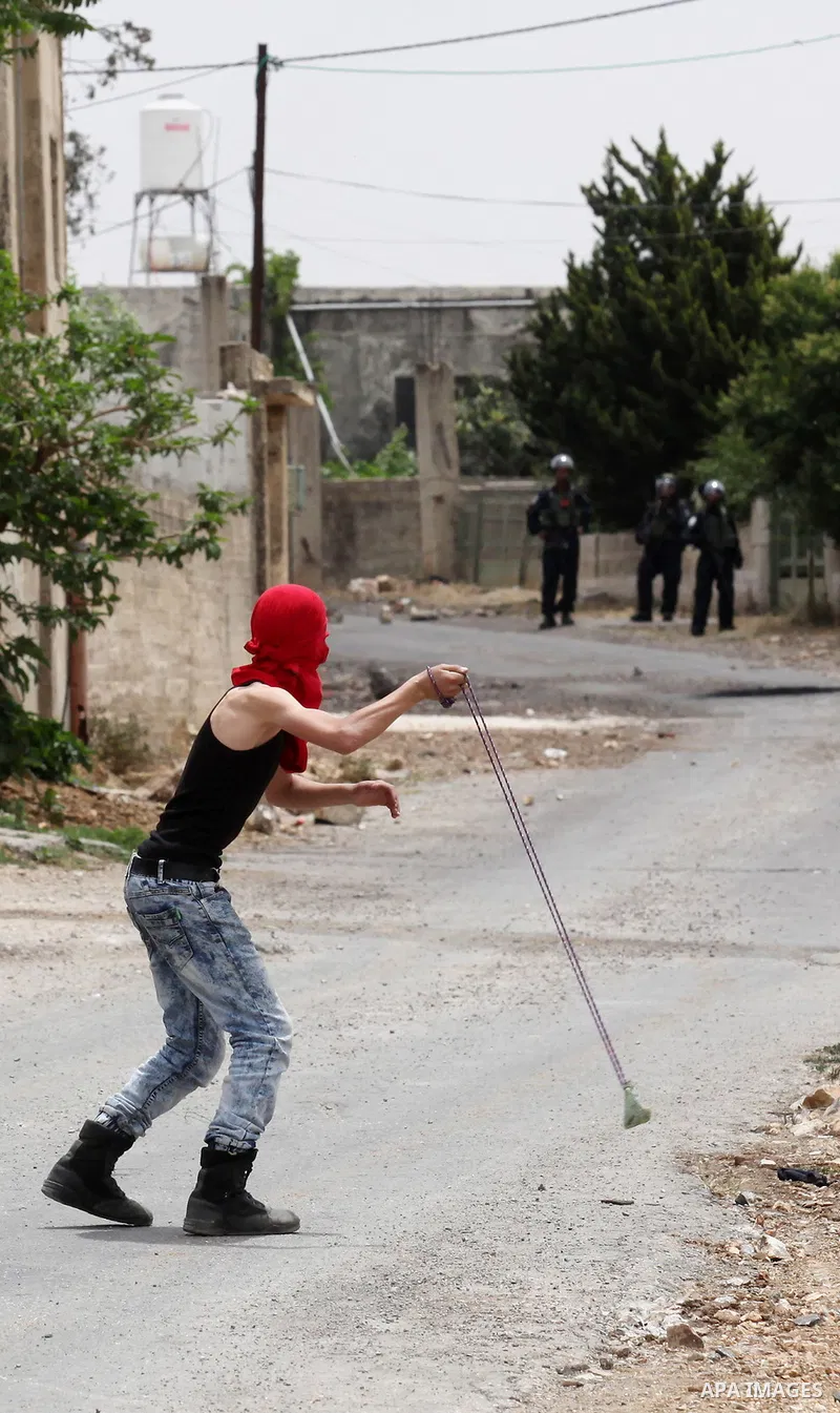 A Palestinian protester uses a slingshot to hurl stones towards Israeli security forces during clashes following a demonstration against the expropriation of Palestinian land by Israel, on May 13, 2016 in the village of...