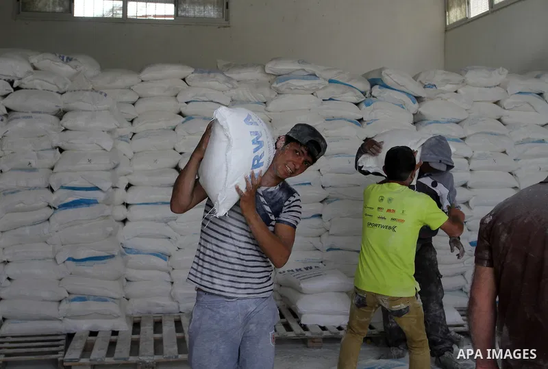 Palestinian workers carry bags of flour to distribute to families, at an aid distribution centre of the United Nations Relief and Works Agency (UNRWA) in the southern Gaza Strip town of Khan Younis on May 15, 2016, on th...