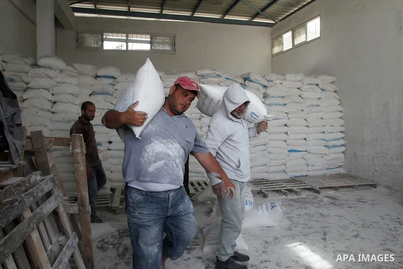 Palestinian workers carry bags of flour to distribute to families, at an aid distribution centre of the United Nations Relief and Works Agency (UNRWA) in the southern Gaza Strip town of Khan Younis on May 15, 2016, on th...