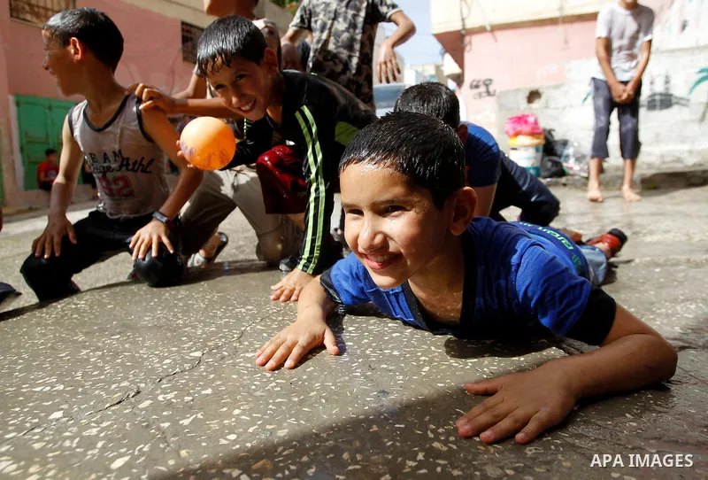 Palestinian children react as they splash water during a sweltering heat wave, at street in al-Fawar Palestinian refugee camp, south of the West Bank city of Hebron on May 15, 2016. Photo by Wisam Hashlamoun