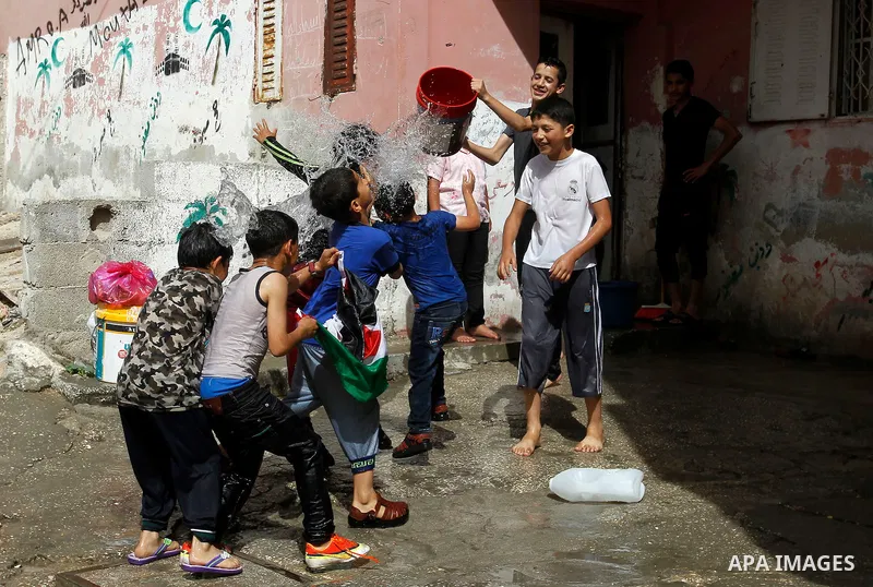 Palestinian children react as they splash water during a sweltering heat wave, at street in al-Fawar Palestinian refugee camp, south of the West Bank city of Hebron on May 15, 2016. Photo by Wisam Hashlamoun