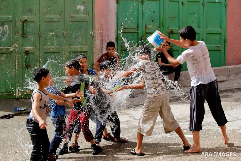 Palestinian children react as they splash water during a sweltering heat wave, at street in al-Fawar Palestinian refugee camp, south of the West Bank city of Hebron on May 15, 2016. Photo by Wisam Hashlamoun