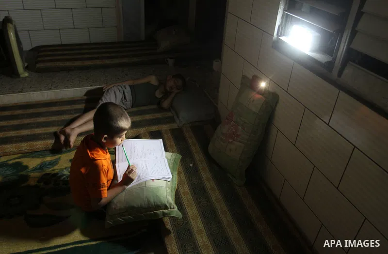 Palestinian boys study on lanterns light during a power outage in Rafah in the southern Gaza Strip on May 18, 2016. Photo by Abed Rahim Khatib