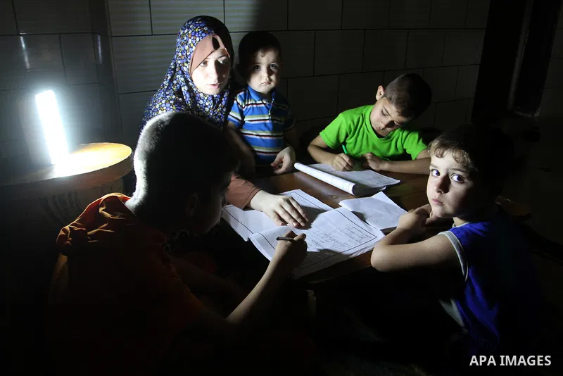 Palestinian boys study on lanterns light during a power outage in Rafah in the southern Gaza Strip on May 18, 2016. Photo by Abed Rahim Khatib
