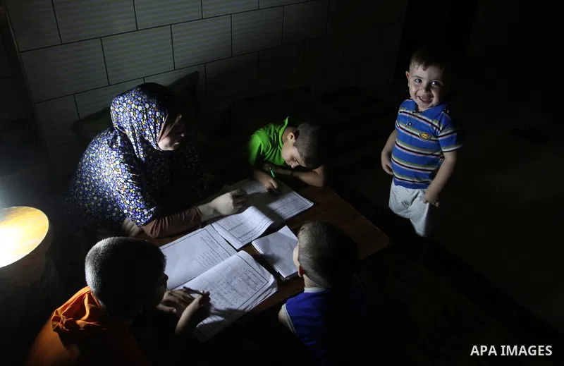 Palestinian boys study on lanterns light during a power outage in Rafah in the southern Gaza Strip on May 18, 2016. Photo by Abed Rahim Khatib