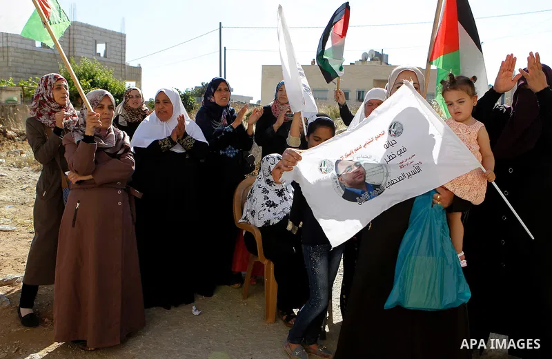 Palestinians wave national flags on May 19, 2016 in the southern West Bank village of Dura, as they wait for the arrival of Palestinian imprisoned journalist, Mohammed al-Qiq, after he was released from the Israeli Nafha...