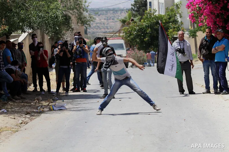 A Palestinian protester uses a slingshot to throw stones towards Israeli security forces during clashes following a demonstration against the expropriation of Palestinian land by Israel, on May 20, 2016 in the village of...