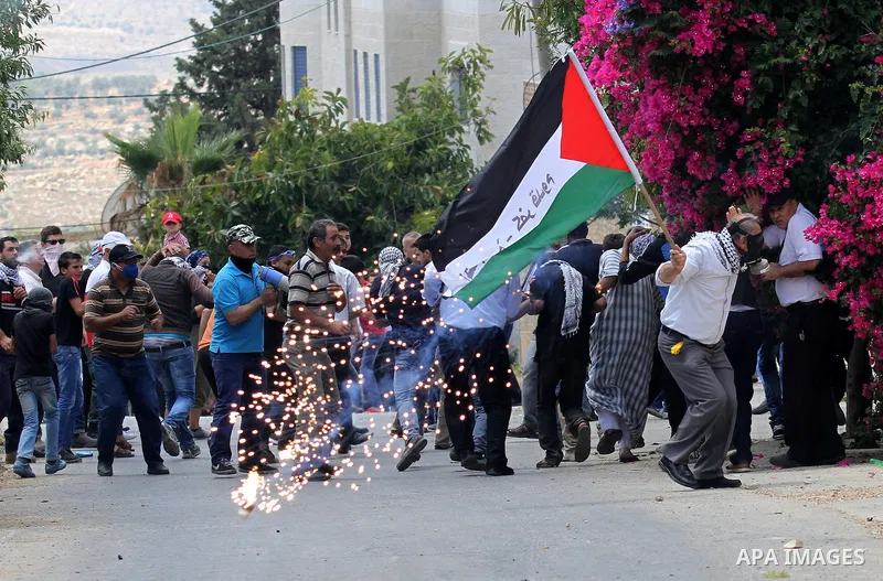 Palestinian protesters take cover from tear gas fired by Israeli security forces during clashes following a demonstration against the expropriation of Palestinian land by Israel, on May 20, 2016 in the village of Kfar Qa...