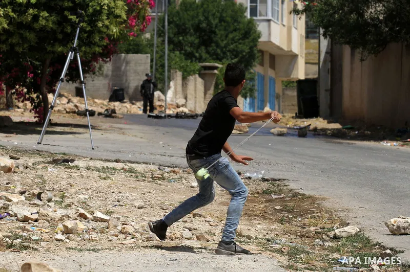 A Palestinian protester uses a slingshot to throw stones towards Israeli security forces during clashes following a demonstration against the expropriation of Palestinian land by Israel, on May 20, 2016 in the village of...