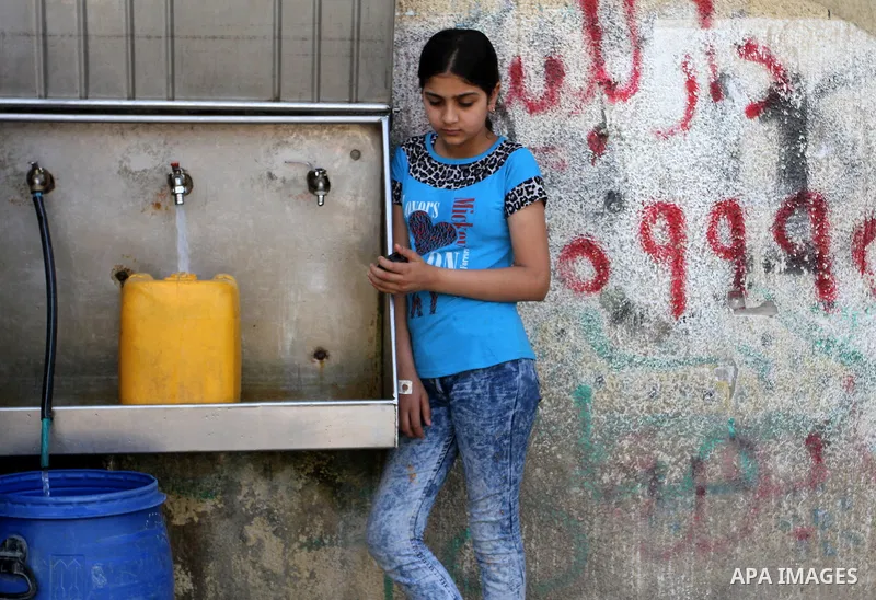A Palestinian girl fills plastic bottles and jerry cans with drinking water from a public tap in Rafah in the southern Gaza strip, on May 22, 2016. Photo by Abed Rahim Khatib