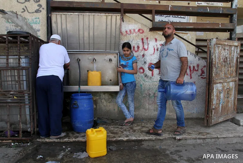 Palestinians fill plastic bottles and jerry cans with drinking water from a public tap in Rafah in the southern Gaza strip, on May 22, 2016. Photo by Abed Rahim Khatib