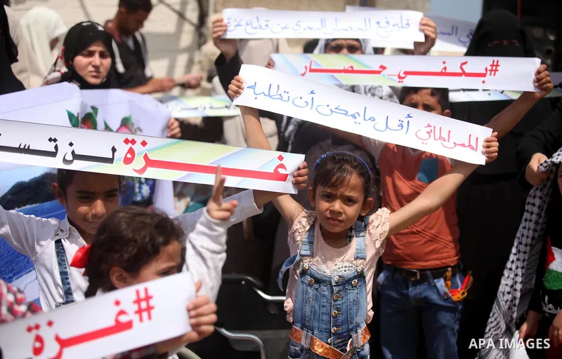 Palestinians hold placards during a protest against the Israeli blockade of the Gaza Strip at the Gaza seaport, on May 24, 2016. Photo by Ashraf Amra