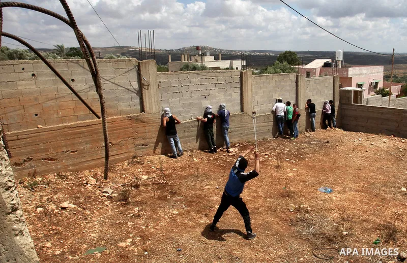 A Palestinian protester uses a slingshot to throw stones towards Israeli security forces during clashes following a demonstration against the expropriation of Palestinian land by Israel, on May 27, 2016 in the village of...