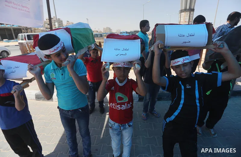 Palestinian children hold banners during a protest to break the siege, at the seaport of Gaza City on 01 June 2016. Photo by Mohammed Asad