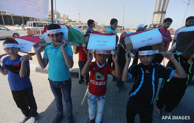 Palestinian children hold banners during a protest to break the siege, at the seaport of Gaza City on 01 June 2016. Photo by Mohammed Asad
