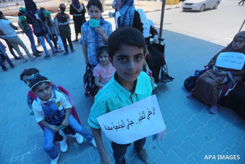 Palestinian children hold banners during a protest to break the siege, at the seaport of Gaza City on 01 June 2016. Photo by Mohammed Asad
