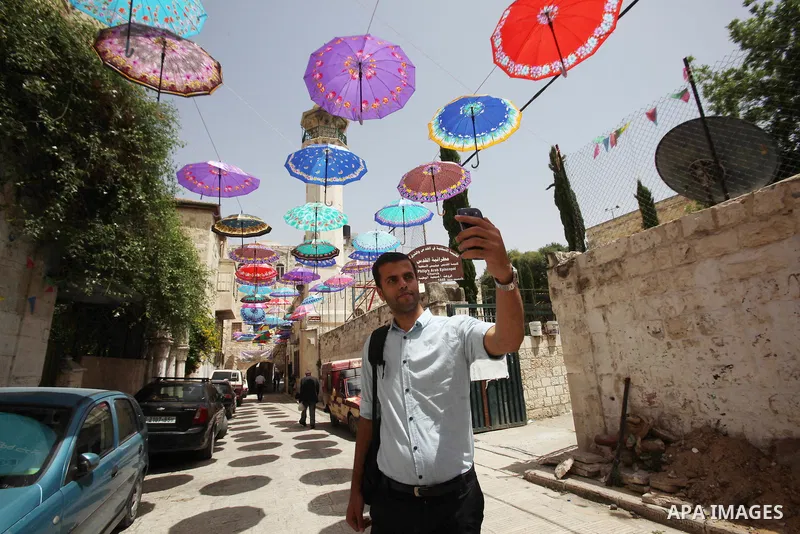 A Palestinian man takes a selfie under show umbrellas used to decorate a street in the Old City of the West Bank town of Nablus, on June 5, 2016 as the faithful prepare to start fasting month of Ramadan. More than 1.5 bi...