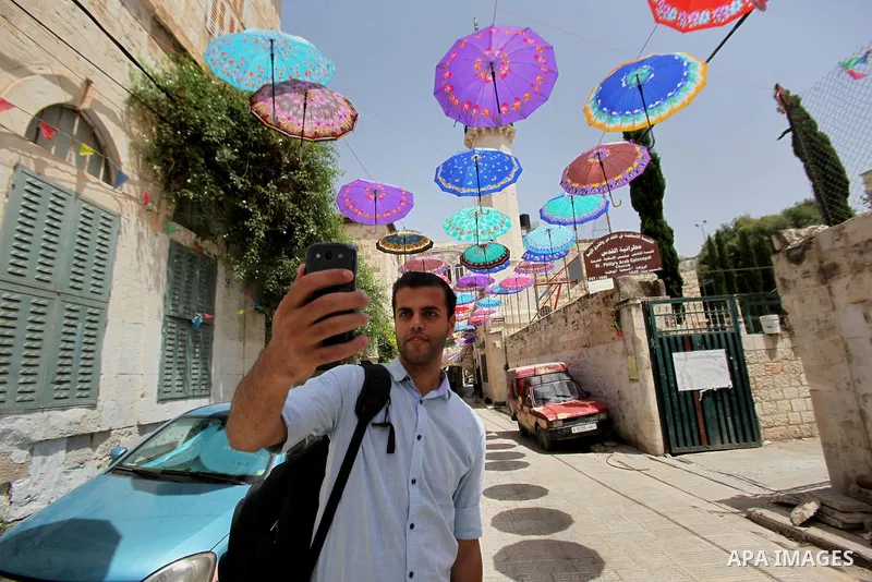 A Palestinian man takes a selfie under show umbrellas used to decorate a street in the Old City of the West Bank town of Nablus, on June 5, 2016 as the faithful prepare to start fasting month of Ramadan. More than 1.5 bi...