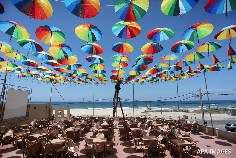 A Palestinian worker of a beachside café shop decorates its terrace with hanging colourful umbrellas as part of decorations for the Muslim holy fasting month of Ramadan in Gaza City, on June 9, 2016. Ramadan is sacred to...