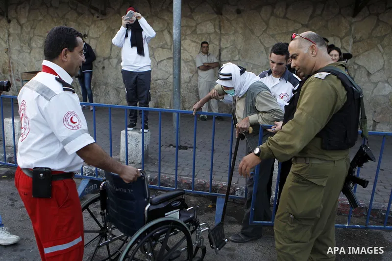 A wheelchair-bound Palestinian man is helped at an Israeli checkpoint as he makes his way to attend the first Friday prayer of the holy fasting month of Ramadan in Jerusalem's al-Aqsa mosque, in the West bank city of Bet...