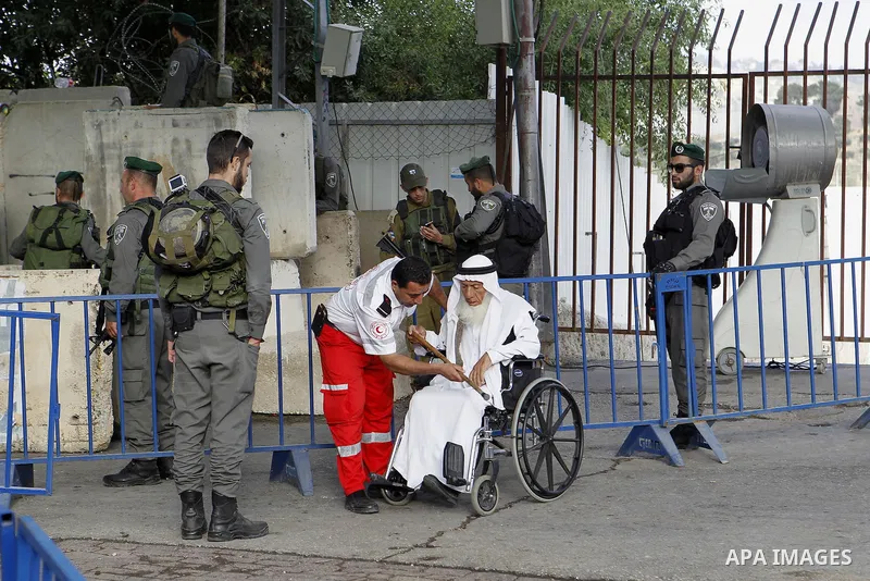 A wheelchair-bound Palestinian man is helped at an Israeli checkpoint as he makes his way to attend the first Friday prayer of the holy fasting month of Ramadan in Jerusalem's al-Aqsa mosque, in the West bank city of Bet...