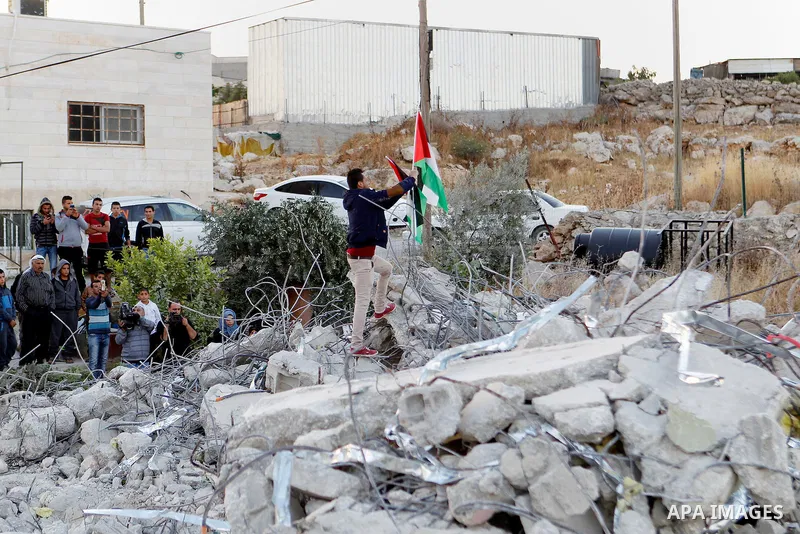 A Palestinian youth holds a Palestinian flag as he stands at the rubble of Palestinian teenager Murad Idais house who was accused of stabbing to death a 38-year old Israeli nurse in an attack in the Israeli Otniel settle...