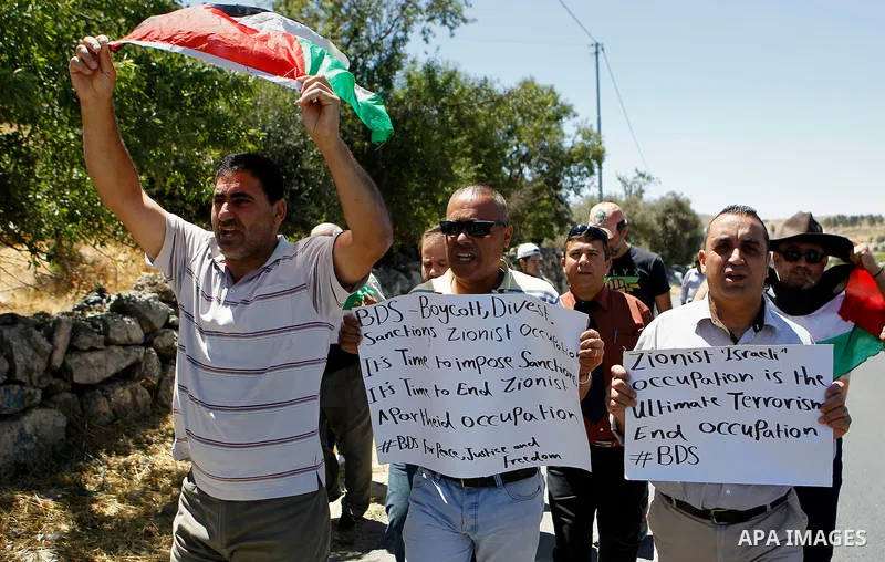 Palestinian protesters hold banners during a protest against what organisers say is land confiscation by Israel, near Arroub refugee camp north of the West Bank city of Hebron June 12, 2016. Photo by Wisam Hashlamoun