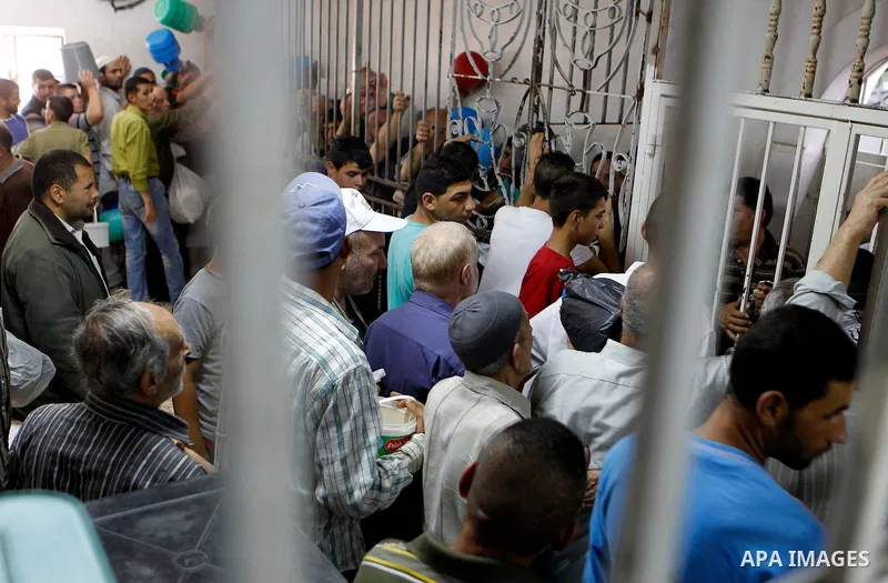 Palestinian families carry containers as they wait to receive free food for 'Iftar', the meal that breaks the daily fast during Ramadan in the West Bank city of Hebron, 13 June 2016. the "Ibrahimi Takiya" was founded in...