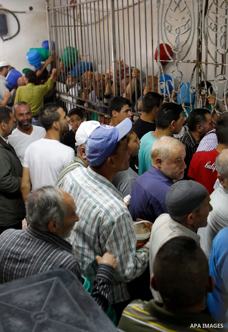 Palestinian families carry containers as they wait to receive free food for 'Iftar', the meal that breaks the daily fast during Ramadan in the West Bank city of Hebron, 13 June 2016. the "Ibrahimi Takiya" was founded in...
