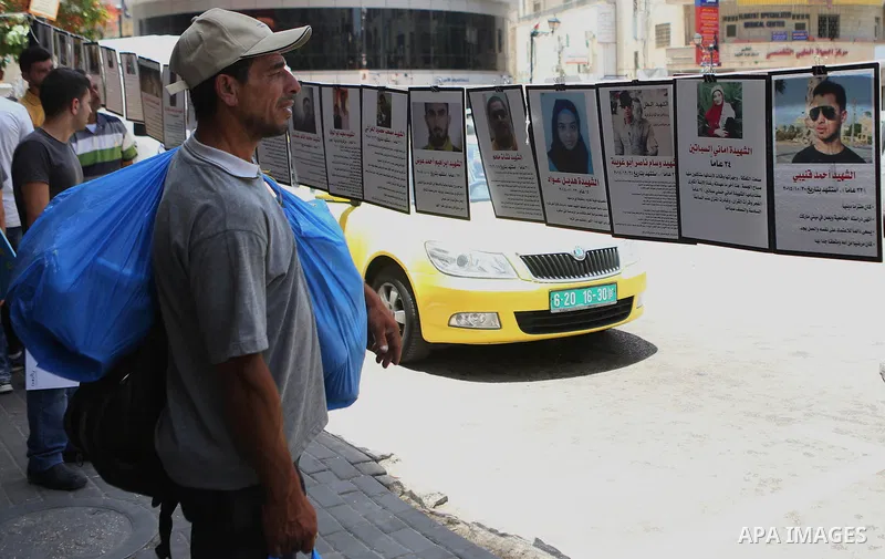 Palestinians walk past posters hanging for martyrs to show solidarity with them, in the West Bank city of Ramallah on June 13, 2016. Photo by Shadi Hatem
