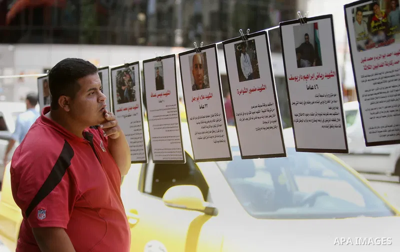 Palestinians walk past posters hanging for martyrs to show solidarity with them, in the West Bank city of Ramallah on June 13, 2016. Photo by Shadi Hatem