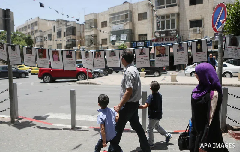 Palestinians walk past posters hanging for martyrs to show solidarity with them, in the West Bank city of Ramallah on June 13, 2016. Photo by Shadi Hatem