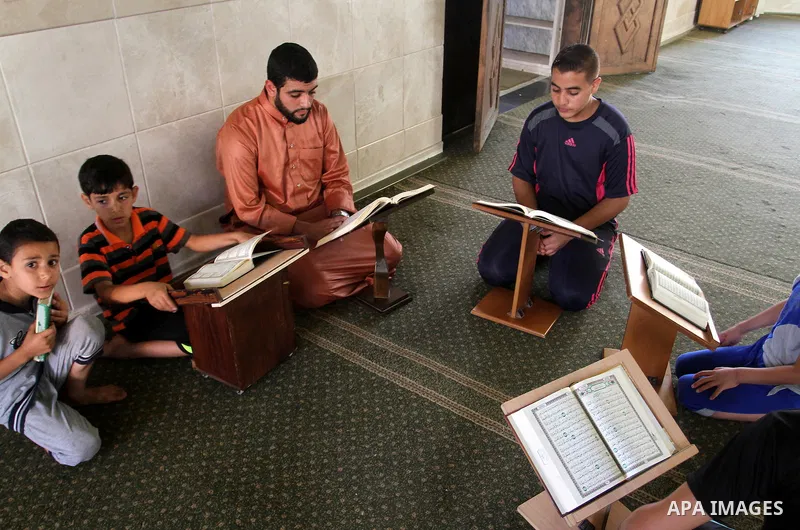 Palestinian men sit reading the Koran, Islam's holy book, at the mosque during the Muslim fasting month of Ramadan, in Rafah in the southern Gaza strip on June 13, 2016. Photo by Abed Rahim Khatib