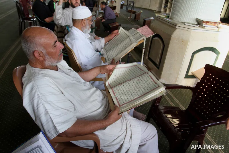Palestinian men sit reading the Koran, Islam's holy book, at the mosque during the Muslim fasting month of Ramadan, in Rafah in the southern Gaza strip on June 13, 2016. Photo by Abed Rahim Khatib