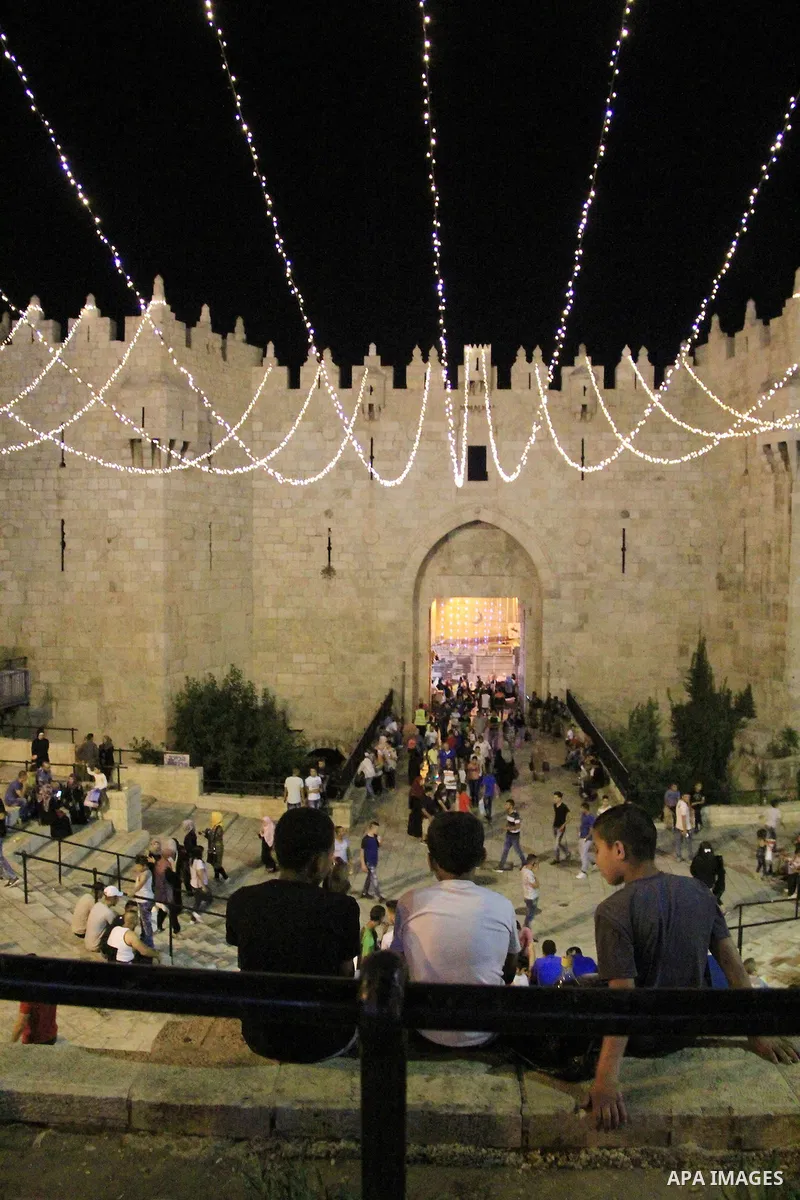 Palestinians walk under lights decorating Damascus Gate following "Taraweeh", nightly prayer of the month of Ramadan, at al-Aqsa mosque, in Jerusalem's old city on June 14, 2016. Ramadan is sacred to Muslims because it i...