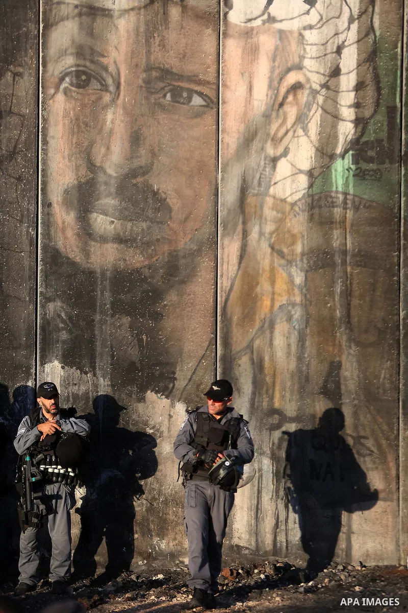 An Israeli border police officer stands guard as Palestinians wait to cross the Qalandia checkpoint between the West Bank city of Ramallah and Jerusalem on June 17, 2016, as they head to Jerusalem's Al-Aqsa mosque for th...