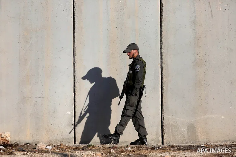 An Israeli border police officer stands guard as Palestinians wait to cross the Qalandia checkpoint between the West Bank city of Ramallah and Jerusalem on June 17, 2016, as they head to Jerusalem's Al-Aqsa mosque for th...