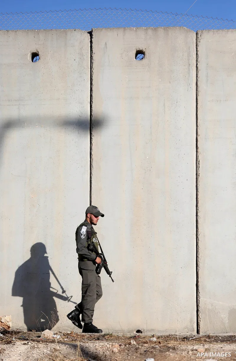 An Israeli border police officer stands guard as Palestinians wait to cross the Qalandia checkpoint between the West Bank city of Ramallah and Jerusalem on June 17, 2016, as they head to Jerusalem's Al-Aqsa mosque for th...