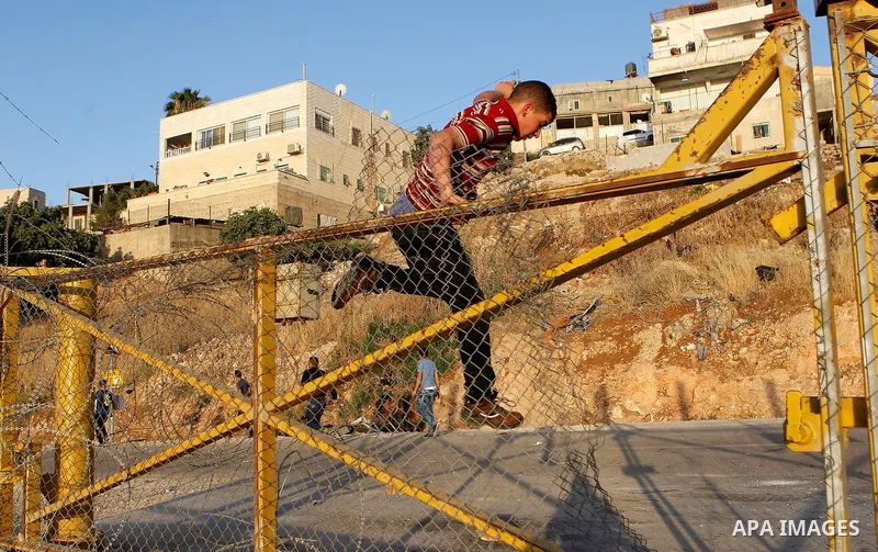 Palestinians, not permitted by Israeli security forces to cross into Jerusalem from the West Bank due to an age limit, climb an Israeli fence between the West Bank town of Bethlehem and Jerusalem as they try to make thei...