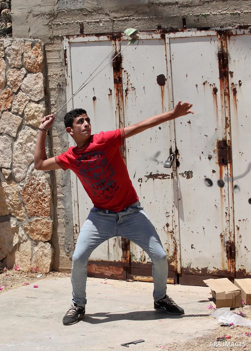 A Palestinian protester uses a slingshot to throw stones towards Israeli security forces during clashes following a demonstration against the expropriation of Palestinian land by Israel, on June 17, 2016 in the village o...