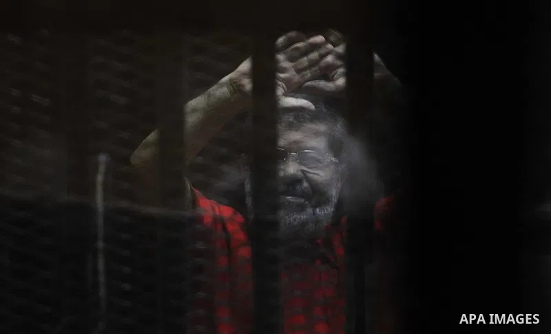 Egypt's ousted Islamist president Mohamed Morsi, wearing a red uniform, looks on from behind the defendant's bars during his trial on espionage charges at a court in Cairo on June 18, 2016. An Egyptian court sentenced Mo...