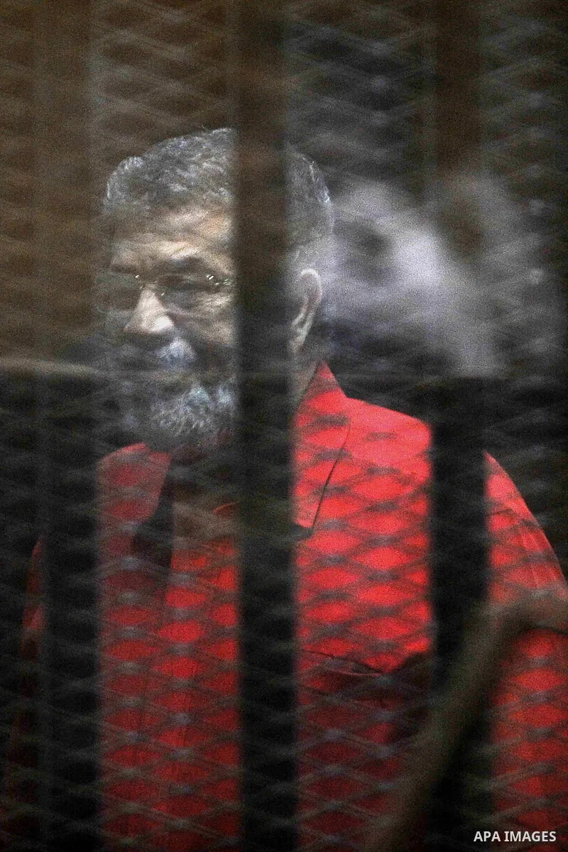 Egypt's ousted Islamist president Mohamed Morsi, wearing a red uniform, looks on from behind the defendant's bars during his trial on espionage charges at a court in Cairo on June 18, 2016. An Egyptian court sentenced Mo...