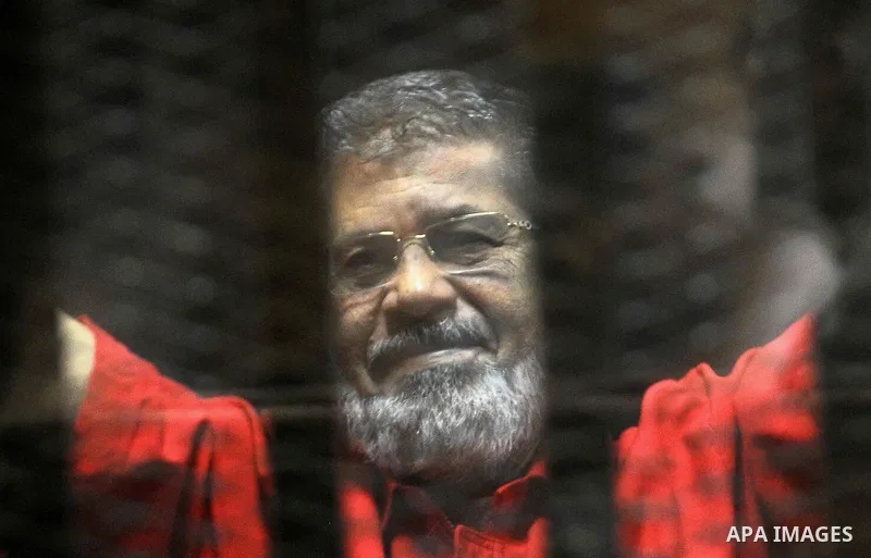 Egypt's ousted Islamist president Mohamed Morsi, wearing a red uniform, looks on from behind the defendant's bars during his trial on espionage charges at a court in Cairo on June 18, 2016. An Egyptian court sentenced Mo...