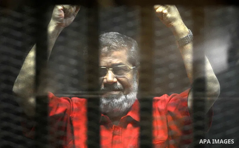 Egypt's ousted Islamist president Mohamed Morsi, wearing a red uniform, looks on from behind the defendant's bars during his trial on espionage charges at a court in Cairo on June 18, 2016. An Egyptian court sentenced Mo...