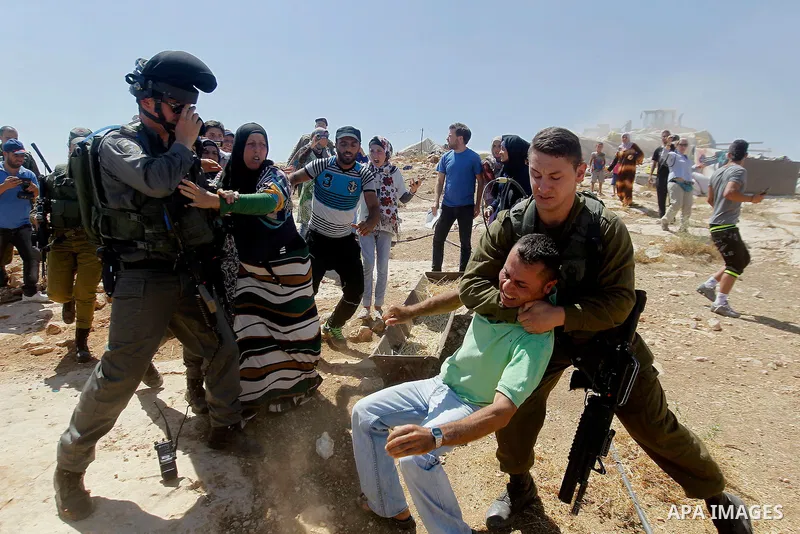 An Israeli soldier grabs a Palestinian man as Israeli troops demolish sheds belonging to Palestinians near the West Bank village of Yatta, south of Hebron June 19, 2016. Photo by Wisam Hashlamoun