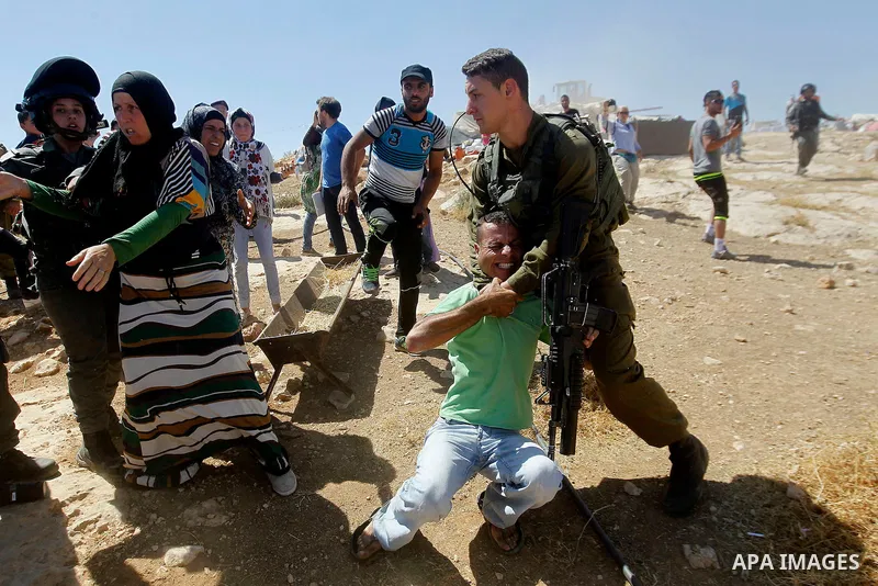 An Israeli soldier grabs a Palestinian man as Israeli troops demolish sheds belonging to Palestinians near the West Bank village of Yatta, south of Hebron June 19, 2016. Photo by Wisam Hashlamoun