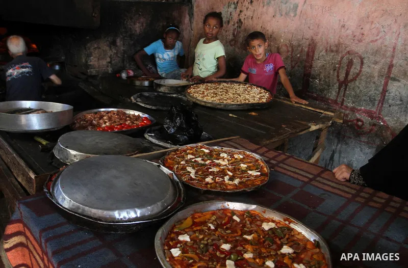 Palestinians wait as they cook their foods in a traditional mud oven during the holy fasting month of Ramadan, in Rafah in the southern Gaza Strip on June 19, 2016. Ramadan is sacred to Muslims because it is during that...