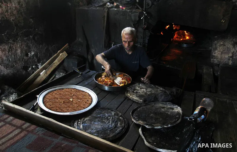 A Palestinian man cooks foods in a traditional mud oven during the holy fasting month of Ramadan, in Rafah in the southern Gaza Strip on June 19, 2016. Ramadan is sacred to Muslims because it is during that month that tr...